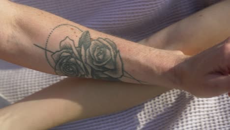Close-up-of-two-arms-intertwined,-one-adorned-with-a-detailed-rose-tattoo,-basking-in-sunlight