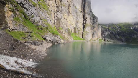 Aerial-flight-next-to-a-beautiful-big-waterfall-on-a-mountain-Landscape,-Drone-Flying-Over-a-Blue-Lake---Oeschinen-Lake,-Switzerland