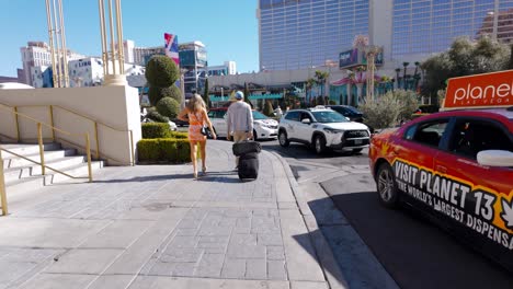 POV-Walking-Behind-Couple-With-Rolling-Luggage-Along-Street-Beside-Taxi-Rank-In-Las-Vegas-On-Sunny-Day