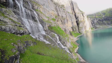 Luftflug-Neben-Einem-Wunderschönen-Großen-Wasserfall-In-Einer-Berglandschaft,-Drohne-Fliegt-über-Einen-Blauen-See---Oeschinensee,-Schweiz