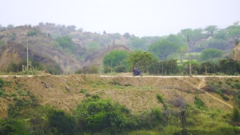 Tracking-shot-of-villagers-on-a-motor-bike-moving-through-a-village-road-in-sem-arid-valley-of-chambal