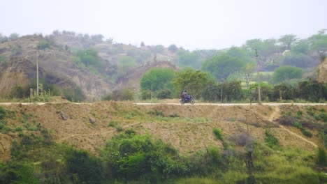 Kamerafahrt-Von-Dorfbewohnern-Auf-Einem-Motorrad,-Die-Durch-Eine-Dorfstraße-Im-Halbtrockenen-Tal-Von-Chambal-Fahren