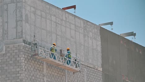 Labourers-are-working-on-a-suspended-platform-at-a-construction-site-in-Dubai,-United-Arab-Emirates