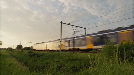 Dutch-Sprinter-Lighttrain-from-NS-passes-at-sunset,-in-direction-of-Amersfoort