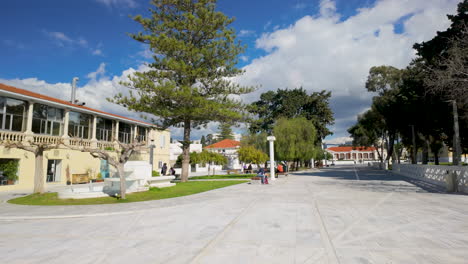 Un-Parque-Público-En-Pafos,-Chipre,-Con-Un-Edificio-De-Dos-Pisos,-árboles-Y-Gente-Disfrutando-Del-Día-Soleado.
