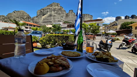 Outdoor-cafe-table-with-Greek-food-and-a-stunning-mountain-backdrop-under-a-bright-blue-sky