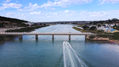 Aerial-riser-view-of-motorboat-speeding-by-on-Goukou-river-under-Stilbaai-bridge