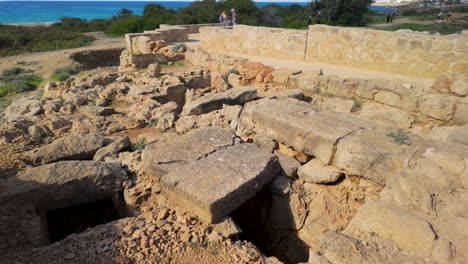 Ruinas-Antiguas-Con-Vistas-Al-Mar-En-Las-Tumbas-De-Los-Reyes-En-Pafos,-Chipre,-Con-Visitantes-Explorando-El-Sitio.
