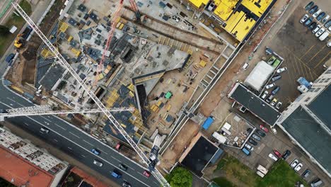 Un-Sitio-De-Construcción-Urbano-Ocupado-Con-Vehículos-Que-Pasan-Por-La-Carretera,-Vista-Aérea