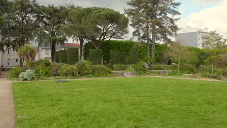 Green-park-in-Nantes,-France-with-trees,-shrubs,-and-people-enjoying-a-walk-on-a-cloudy-day