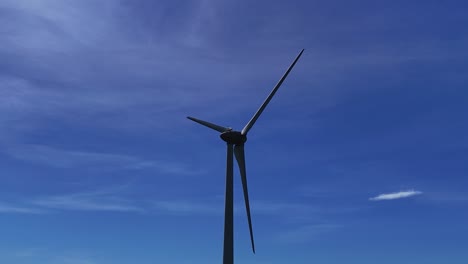 Turbina-Eólica-Girando-Bajo-Un-Cielo-Azul-Brillante,-Tomada-Desde-Un-ángulo-Bajo