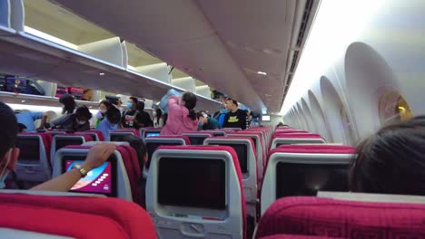 Panning-shot-of-Chinese-travelers-inside-aircraft-placing-hand-luggage-in-cabin,-Beijing-Capital-airport-during-Covid-19-pandemic