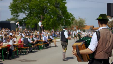 Traditionelles-Bayerisches-Maifest-Mit-Musikern,-Menschen,-Maibaum,-Peitschen,-Lederhosen