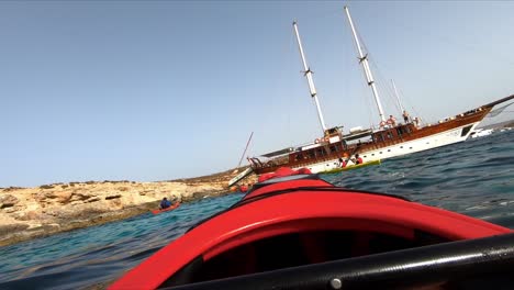 A-group-of-kayaking-people-paddles-around-a-traditional-Maltese-sailing-boat-in-the-Mediterranean-Sea-off-the-coast-of-Comino
