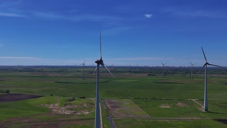 Wind-turbines-spinning-on-a-sunny-day-in-a-vast-green-field,-aerial-view