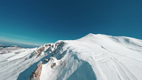 Snow-covered-mountain-peak-under-clear-blue-sky,-aerial-view