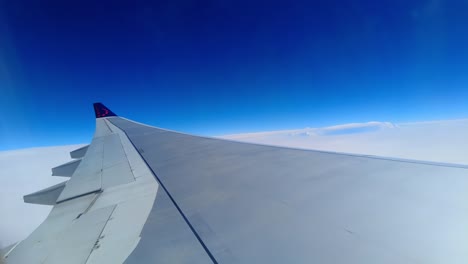 Blick-Auf-Den-Flugzeugflügel-Mit-Wunderschönen-Schneeweißen-Wolken-Und-Tiefblauem-Himmel-An-Einem-Sonnigen-Tag,-Aufgenommen-Durch-Das-Flugzeugfenster