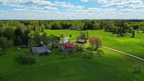 Schönes-Kleines-Bauernhaus-Mit-Riesigen-Grünen-Wiesen-Und-Wäldern-In-Lettland,-Luftaufnahme