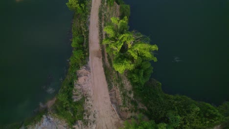 Drone-flying-over-a-lake-and-dirt-road-with-a-tracto