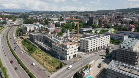 Eine-Drohne-Fliegt-Langsam-Von-Einer-Baustelle-Mit-Neu-Errichteten-Strukturen-Weg-Und-Enthüllt-Die-Skyline-Einer-Wunderschönen-Stadt-In-Der-Schweiz