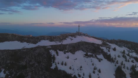 Corno-bianco-mountain-at-sunset-with-patches-of-snow-and-a-cross-on-the-summit,-aerial-view