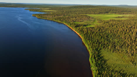 Drone-tilting-away-from-a-red-sand-beach-at-lake-Pallasjarvi,-sunset-in-Lapland