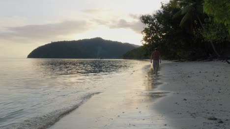 A-man-walks-along-the-sandy-beach-of-Kri-Island-in-the-Raja-Ampat-archipelago,-Indonesia