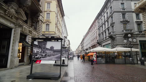 Día-Lluvioso-En-Milán-Mostrando-Una-Calle-Comercial-Con-Una-Exposición-Histórica-Y-Un-Ciclista.