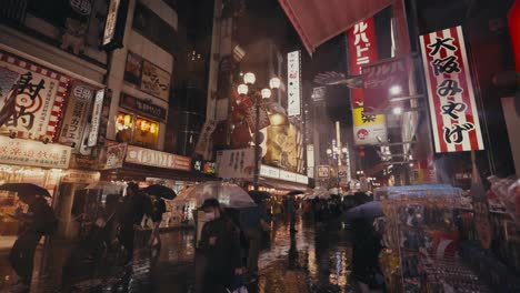 Gente-Con-Paraguas-En-Una-Noche-Lluviosa-En-El-Centro-De-Osaka-En-Japón