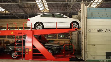 Cars-loaded-onto-a-red-double-decker-car-transporter-train-in-an-industrial-facility