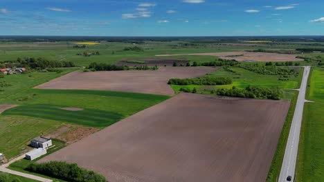 Expansive-farmland-with-fields-and-roads-on-a-sunny-day,-aerial-view