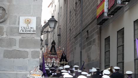 A-"paso"-float-rocking-gently-in-the-distance-as-it-is-carried-through-Madrid,-followed-by-a-marching-band-during-the-Easter-celebrations