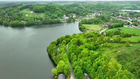 A-broad-aerial-view-of-a-lakeside-town-surrounded-by-green-hills,-showing-houses,-roads,-and-a-tranquil-lake