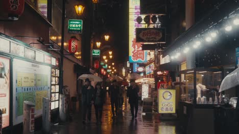 Turistas-Con-Sombrillas-Caminando-Bajo-La-Lluvia-Por-La-Noche-En-La-Calle-De-Osaka,-Japón