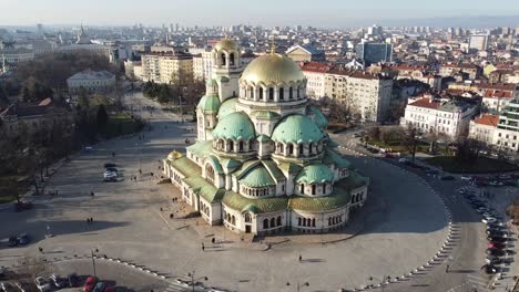 Aerial-orbital-drone-clip-circling-around-Alexander-Nevsky-Cathedral-clockwise-in-the-Winter-sun-with-the-city-of-Sofia-and-Stara-Planina,-Bulgaria-in-the-background