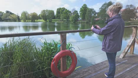 Female-Tourist-takes-snapshot-of-Diss-park-lake-from-boardwalk-with-lifebouy-ring