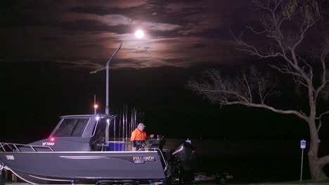 A-serene-night-scene-featuring-a-radiant-full-moon-shining-brightly-on-a-boat-perched-atop-a-trailer-near-the-riverside