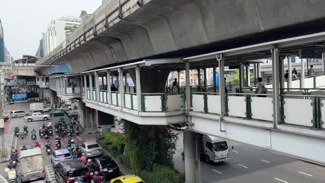 Busy-road-traffic-and-the-commuters-walking-on-the-overhead-sky-bridge-in-Bangkok,-Thailand