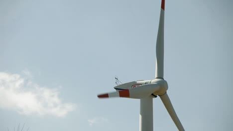 Close-up-of-a-wind-turbine-against-a-clear-blue-sky,-blades-rotating-slowly