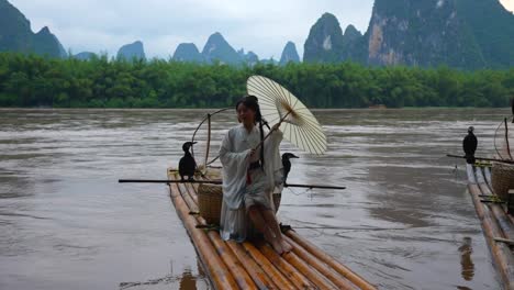 Hanfu-Mädchen-Mit-Regenschirm-Auf-Bambusfloß-In-Xingping-Posiert-Mit-Kormoranen