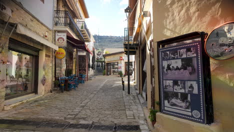 A-cobblestone-street-in-Lefkara,-Cyprus,-lined-with-shops-and-cafes,-with-mountains-in-the-background
