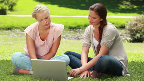 Zwei-Mädchen-Benutzen-Einen-Laptop,-Während-Sie-Im-Park-Sitzen-Und-Dann-In-Die-Kamera-Schauen