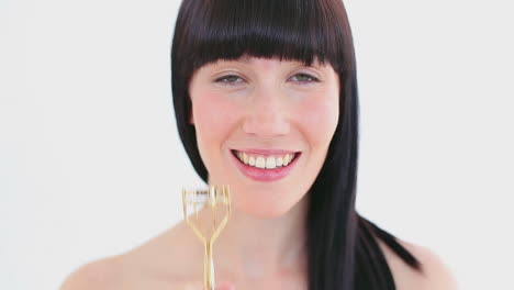 Smiling-brunette-using-a-curler-for-her-eyelashes