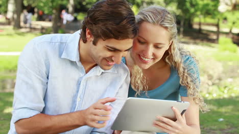 A-couple-use-a-tablet-together-as-they-then-look-at-the-camera