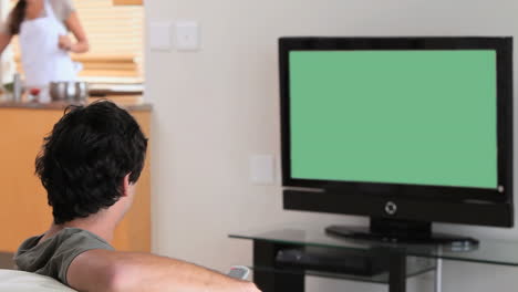 Man-watching-the-television-while-his-wife-is-cooking