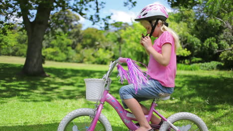 Ein-Mädchen-Nimmt-Ihren-Helm-Aus-Einem-Fahrradkorb-Und-Setzt-Ihn-Auf-Den-Kopf,-Während-Sie-Auf-Dem-Fahrrad-Sitzt