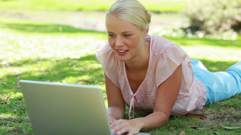 Una-Mujer-Tumbada-En-El-Parque-Con-Su-Computadora-Portátil-Mientras-Mira-A-La-Cámara