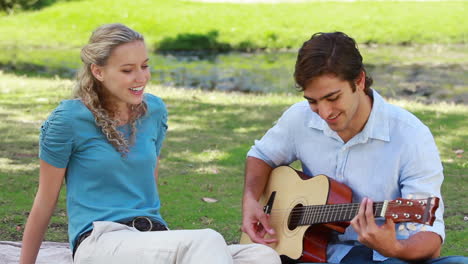 Ein-Mann-Spielt-Gitarre-Und-Singt-Einer-Frau-Etwas-Vor,-Während-Sie-Im-Park-Sitzen