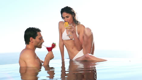 Couple-holding-cocktail-glasses-in-a-swimming-pool