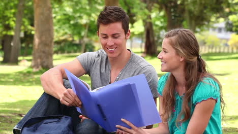 Two-friends-laughing-while-pointing-at-a-folder-as-they-sit-together